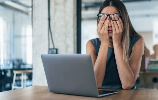A sad adult woman wearing glasses working on a laptop.
